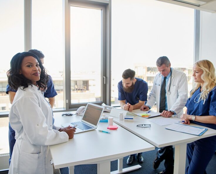 Black female doctor smiling at camera during a meeting with other doctors